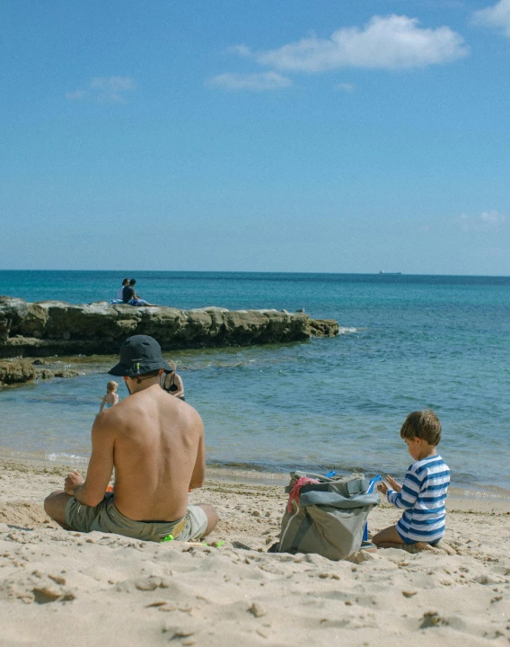 a man sitting next to a little boy on a beach, by Carey Morris, pexels contest winner, lgbtq, great barrier reef, spying discretly, al fresco