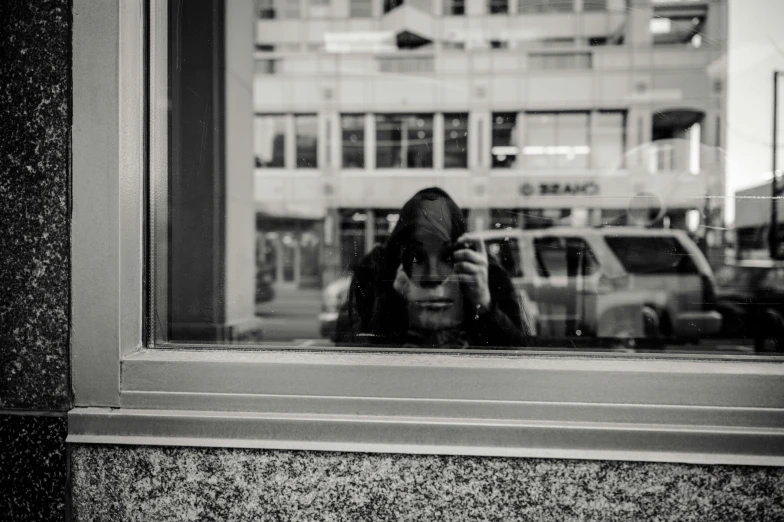 a woman taking a picture of herself through a window, a black and white photo, realism, covered face, on a sidewalk of vancouver, candid photography, hiding behind obstacles