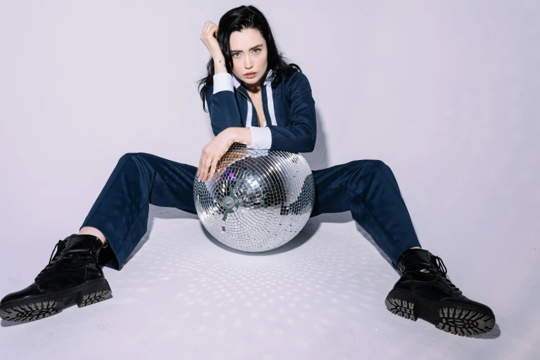 a woman sitting on the floor with a disco ball, pale skin, wearing a track suit, press shot, rey