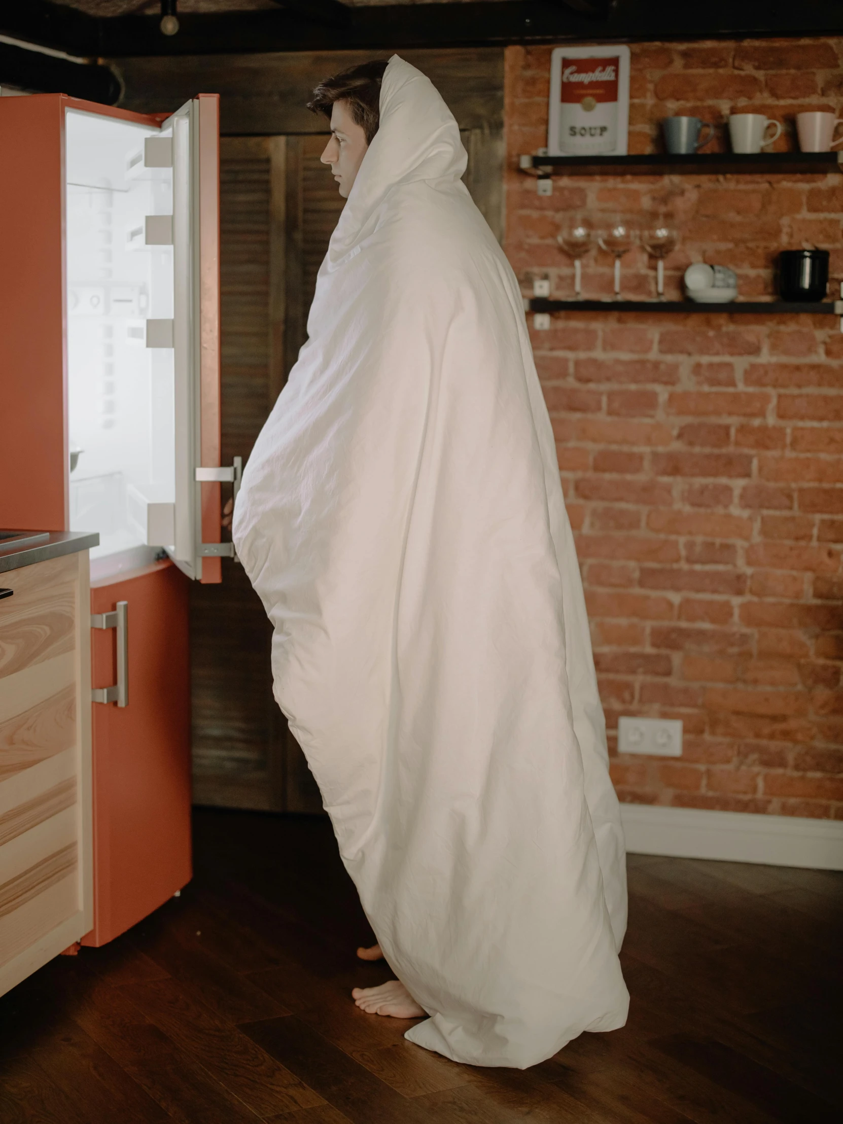 a man standing in front of an open refrigerator, an album cover, by Andrew Stevovich, unsplash, very long white cloak, covered with blanket, facing away from camera, full body with costume