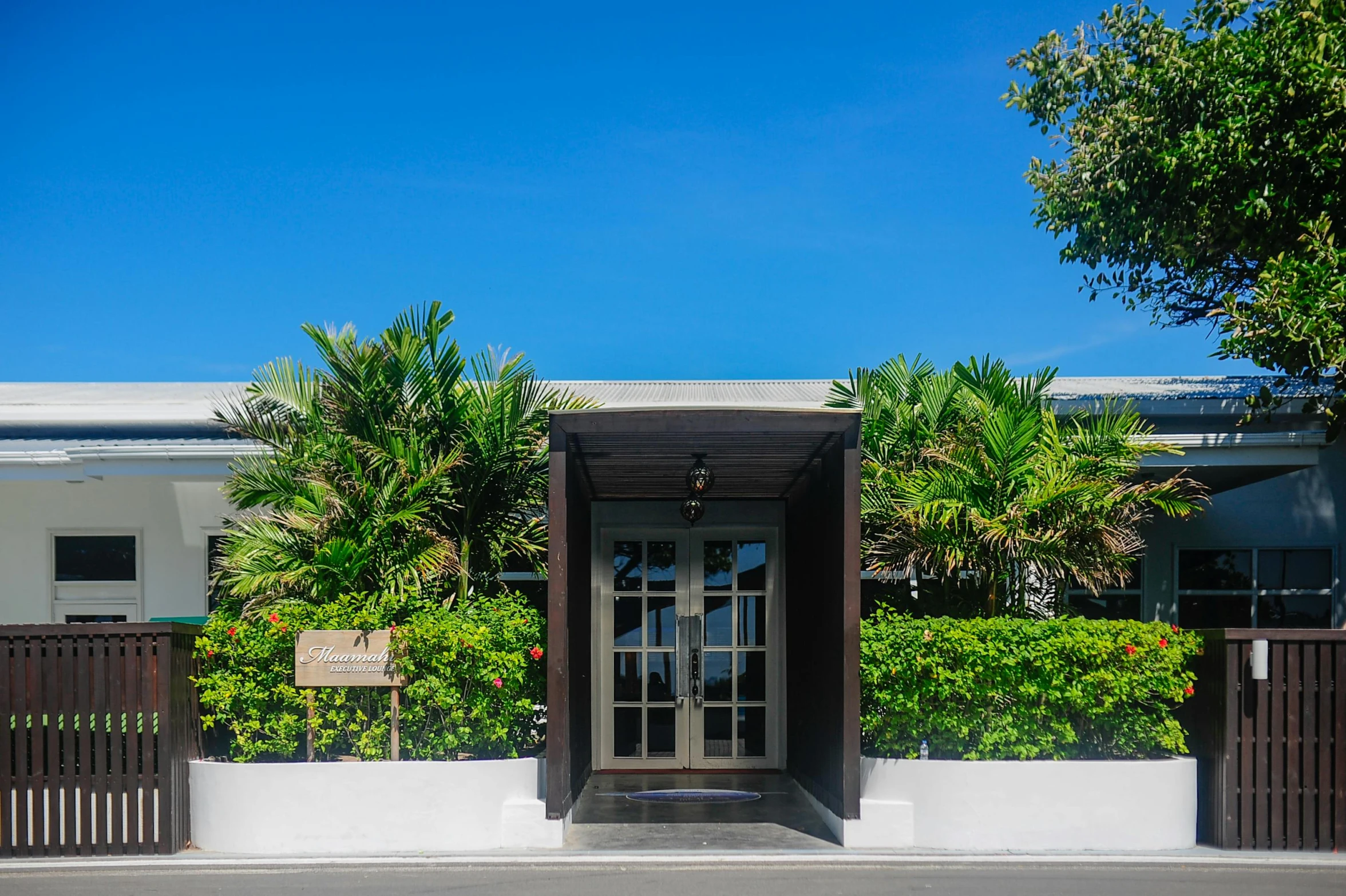 a building with a bunch of plants in front of it, tropical trees, entrance, michelin star restaurant, exterior photo