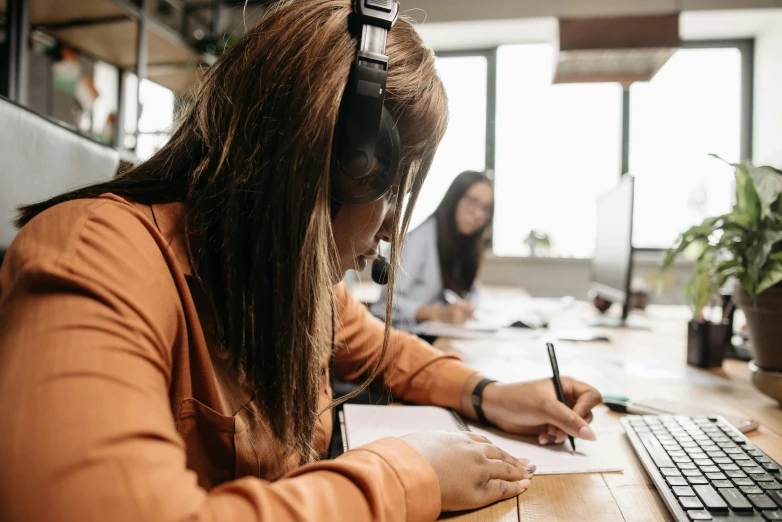 a woman sitting at a desk in front of a computer, trending on pexels, with head phones, pencil and paper, thumbnail, coworkers