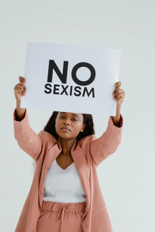 a woman holding a sign that says no sexism, trending on pexels, essence, brown, profile picture, struggling