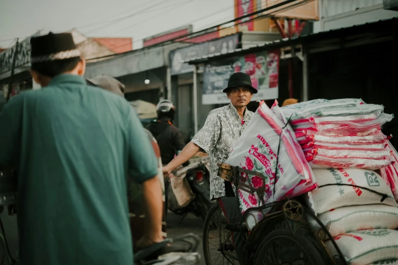 a man riding a bike down a street next to a pile of bags, pexels contest winner, pink, farmer, people watching around, avatar image