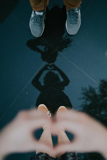 a person making a heart shape with their hands, pexels contest winner, sitting on a reflective pool, standing on two feet, shadowy figures, upsidedown