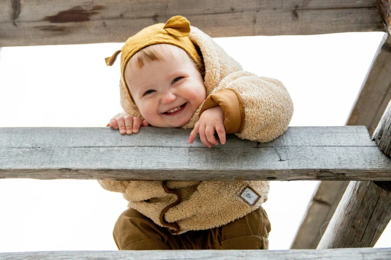 a small child standing on top of a wooden structure, inspired by Margaret Geddes, unsplash, mingei, cuddly fur, smiling down from above, close up details, in a hoodie