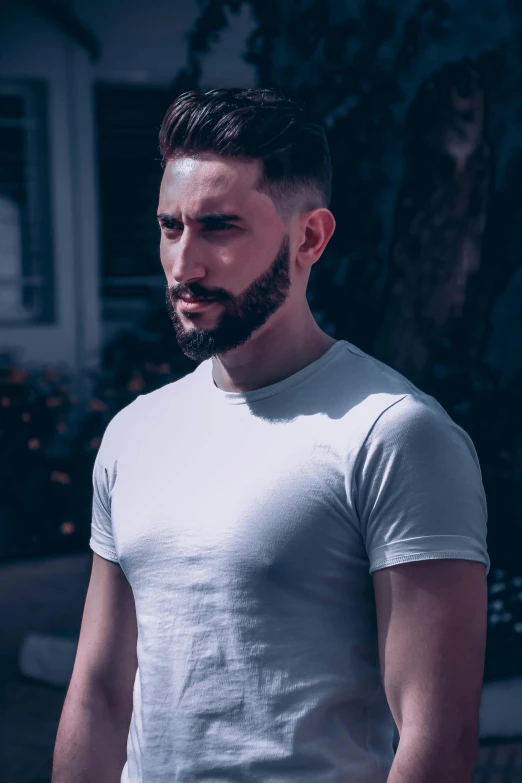 a man with a beard standing in front of a house, a colorized photo, inspired by Camilo Egas, pexels contest winner, wearing tight shirt, non binary model, dressed in a white t-shirt, dark backdrop