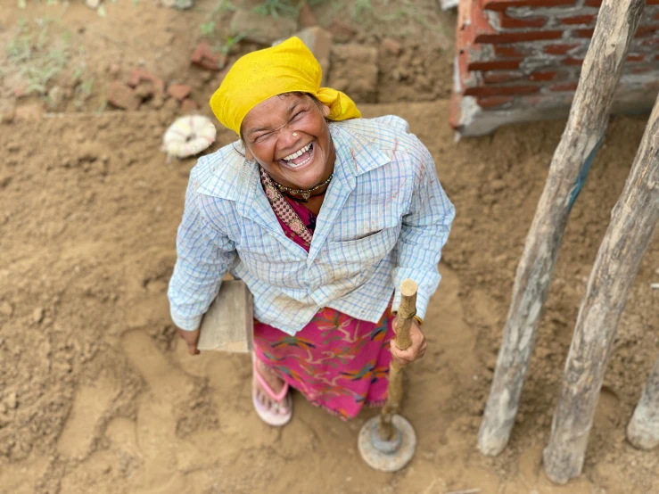 a woman that is standing in the dirt, smiling down from above, nepal, holding a cane, full device