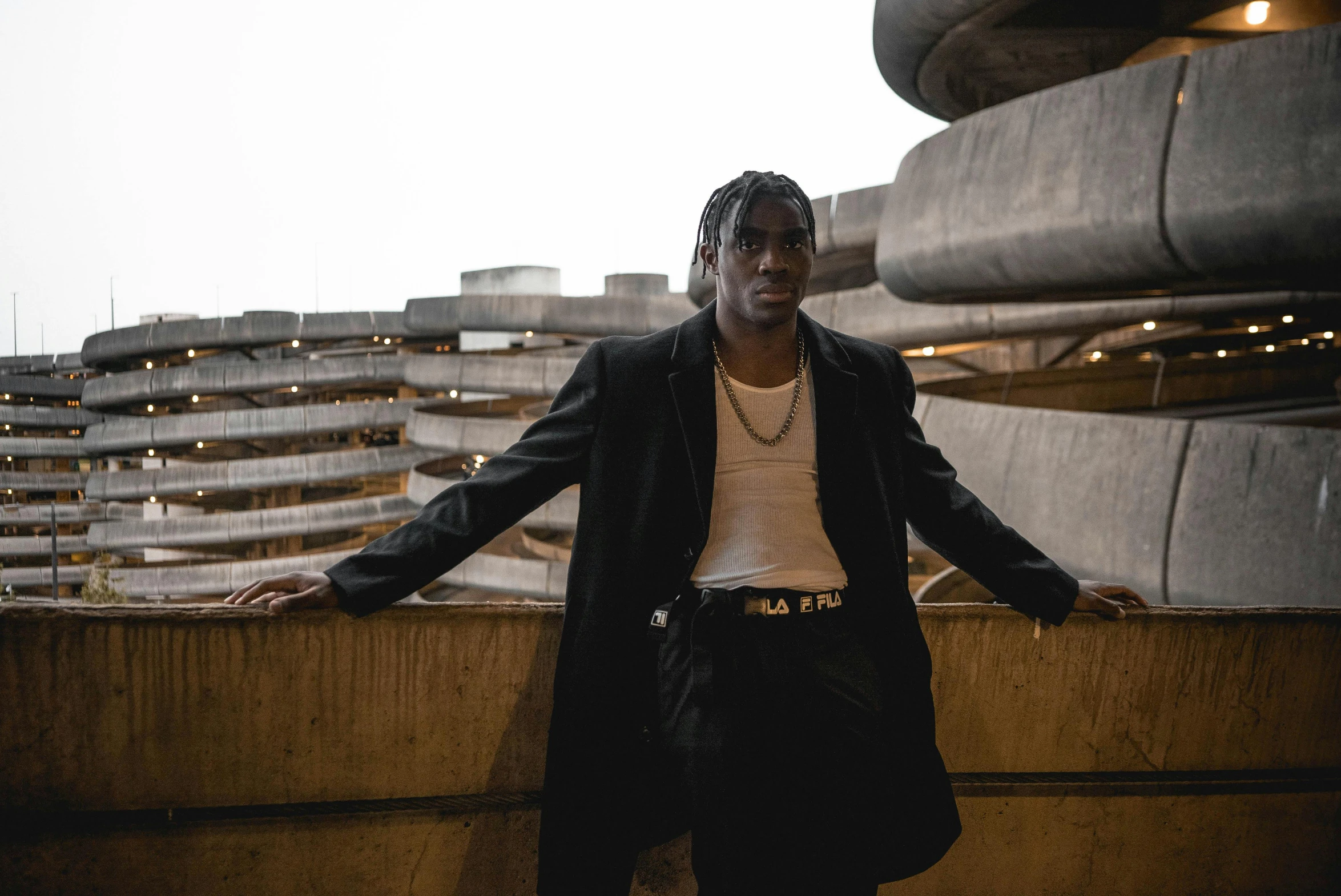 a man standing on a ledge in front of a building, an album cover, pexels contest winner, lil uzi vert, elegant pose, androgynous person, standing in an arena