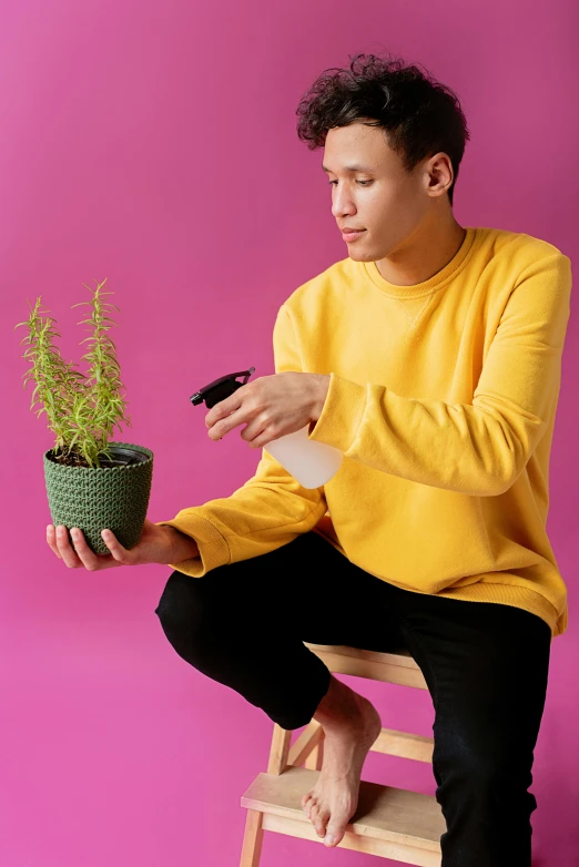 a man sitting on a stool holding a potted plant, an album cover, inspired by Russell Dongjun Lu, trending on unsplash, pink shirt, holding flask in hand, non binary model, herbs