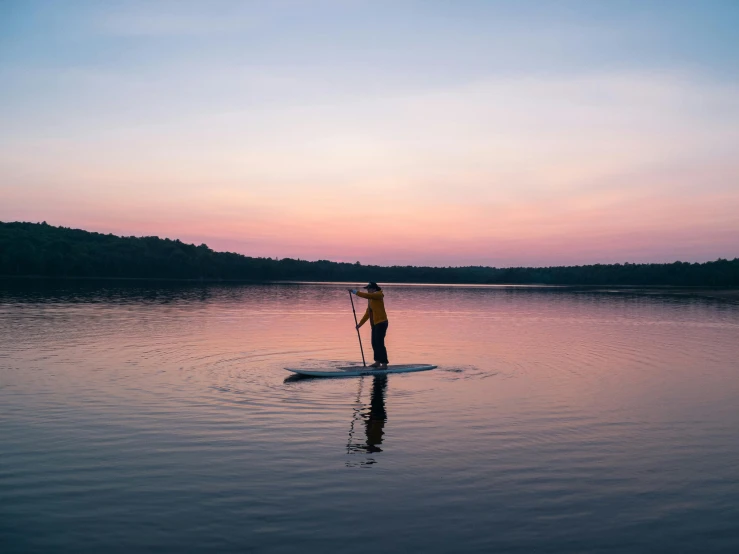 a man riding a paddle board on top of a lake, by Carey Morris, unsplash contest winner, minimalism, pink golden hour, minn, standing straight, afternoon hangout