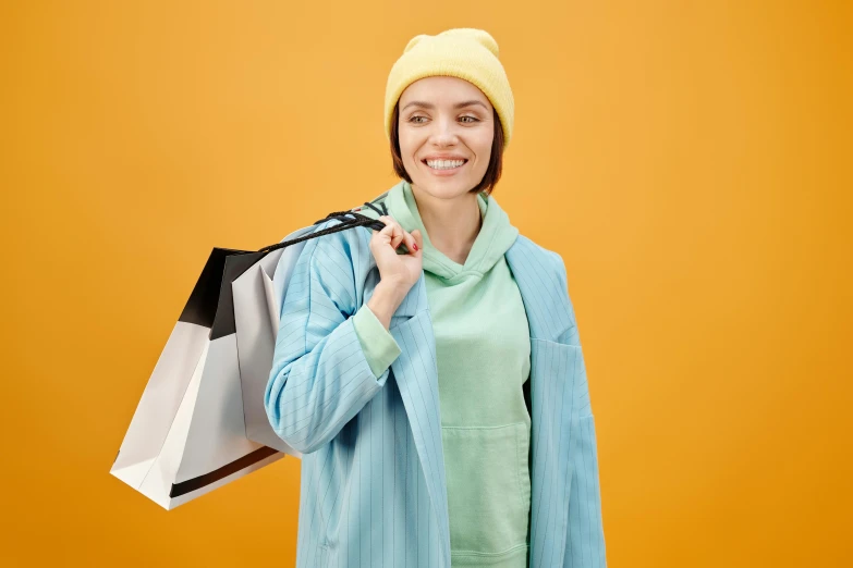 a woman holding shopping bags and smiling at the camera, a colorized photo, trending on pexels, happening, wearing a yellow hoodie, ferred - themed robes and hat, avatar image, full product shot