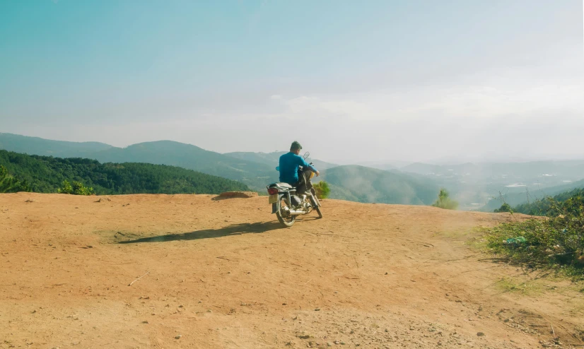 a man riding a motorcycle down a dirt road, pexels contest winner, figuration libre, on the top of a hill, patiphan sottiwilaiphong, avatar image, distant full body view