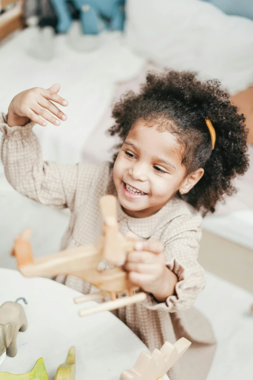 a little girl sitting at a table playing with wooden toys, pexels contest winner, renaissance, african american young woman, smiling down from above, raising an arm, closeup of an adorable