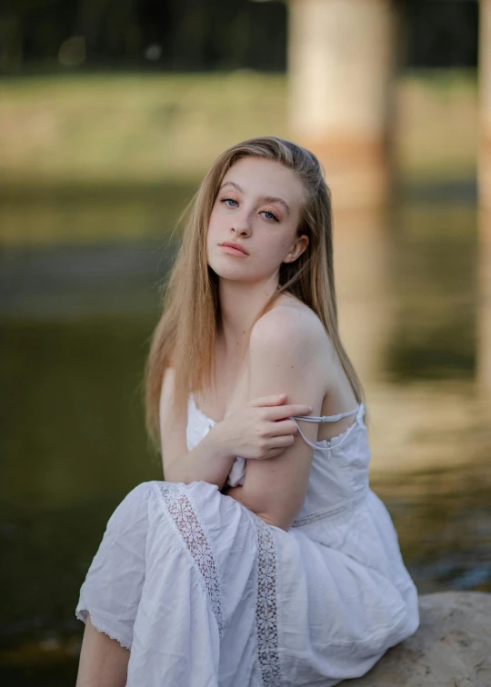 a woman sitting on a rock near a body of water, a picture, inspired by Albert Edelfelt, unsplash, renaissance, wearing a cute white dress, headshot, 1 6 years old, medium format. soft light