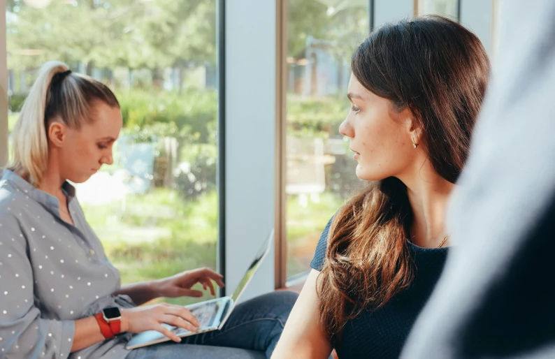 two women sitting next to each other with laptops, by Lisa Milroy, trending on unsplash, “ iron bark, next to a big window, healthcare, calmly conversing 8k