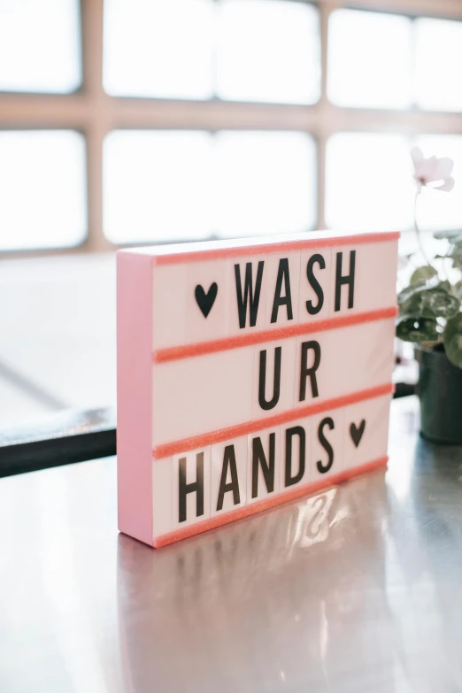 a sign that says wash your hands next to a potted plant, by Julia Pishtar, trending on unsplash, soft pink lights, back of hand on the table, light box, 1 6 x 1 6