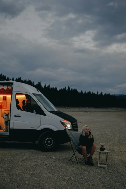 a man sitting on a chair in front of a van, by Tom Bonson, trending on unsplash, renaissance, montana, late evening, high quality photo, wide long view