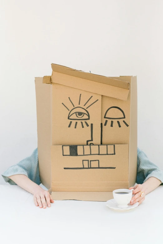 a person sitting at a table with a cardboard box on their head, inspired by Saul Steinberg, trending on unsplash, happy face, made of cardboard, ilustration, full view of face and body