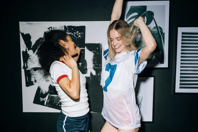 a couple of women standing next to each other, a photo, by Julia Pishtar, unsplash contest winner, graffiti, celebrate goal, indoor picture, wearing shorts and t shirt, wearing white leotard