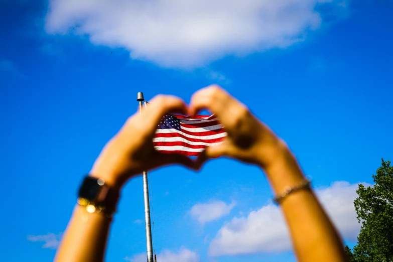 a person holding an american flag in front of a blue sky, by Julia Pishtar, unsplash, avatar image, love peace and unity, blurred photo, 🚿🗝📝