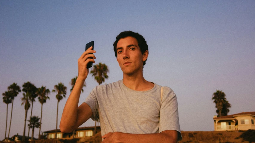 a man taking a picture with his cell phone, an album cover, by Carey Morris, unsplash contest winner, serial art, lean man with light tan skin, early evening, looking off to the side, portrait of tall