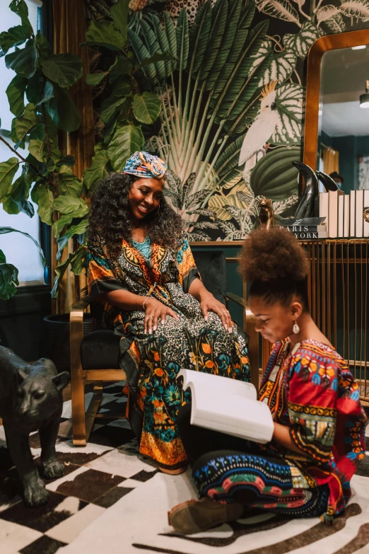 two women sitting on a black and white checkered floor, by Ingrida Kadaka, pexels contest winner, afrofuturism, reading a book next to a lion, adorned with all kind of plants, somali attire, with afro