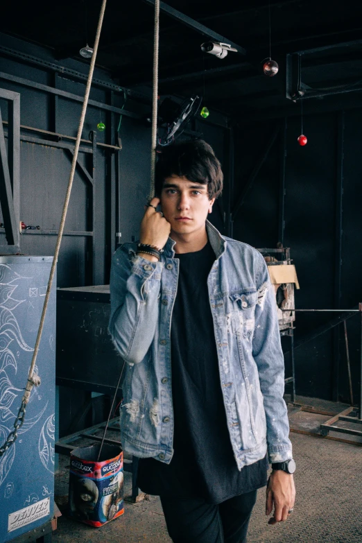 a man standing in a room talking on a cell phone, an album cover, inspired by John Luke, graffiti, wearing a jeans jackets, he is wearing a black t-shirt, headshot profile picture, tense look