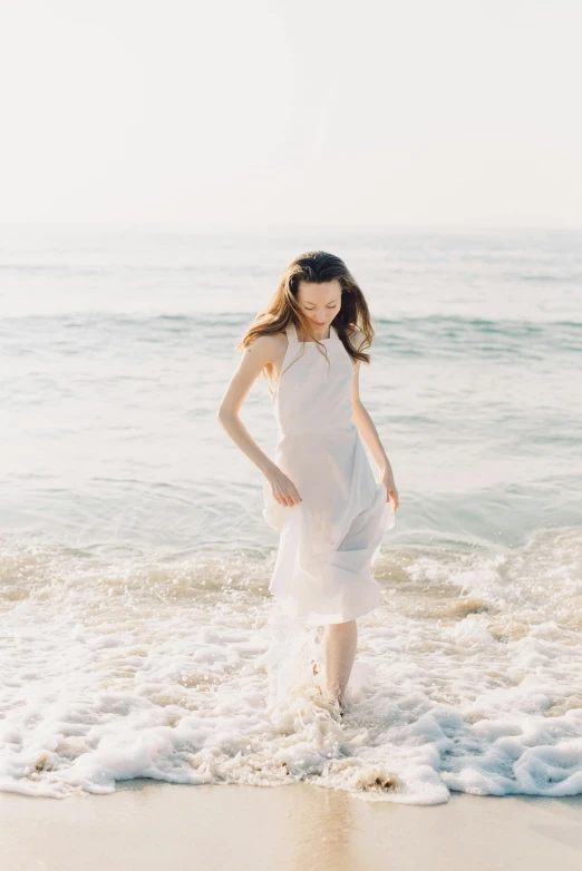 a woman standing on top of a beach next to the ocean, wearing organza gown, pale fair skin, soaring waves, saltwater