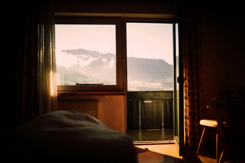 a bed sitting in a bedroom next to a window, a picture, by Sebastian Spreng, trending on unsplash, happening, sunshine lighting high mountains, balcony door, late summer evening, hotel room