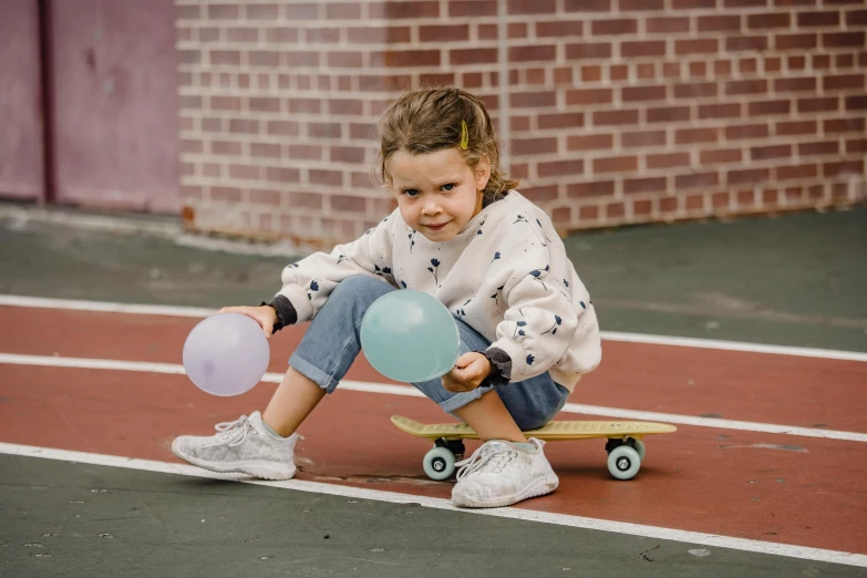 a little girl sitting on a skateboard with a bunch of balloons, by Emma Andijewska, pexels contest winner, holding a ball, denim, casual game, soft surfaces