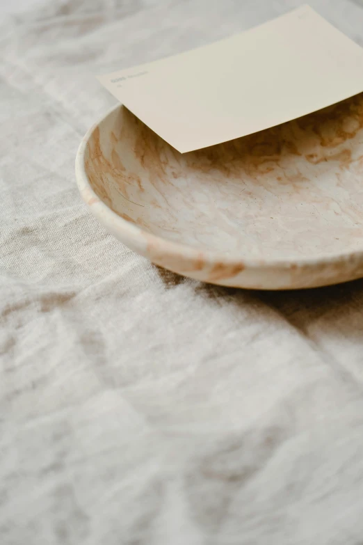 a piece of paper sitting on top of a plate, a marble sculpture, by Rebecca Horn, trending on unsplash, wooden bowl, soft surface texture, textiles, subtle pattern