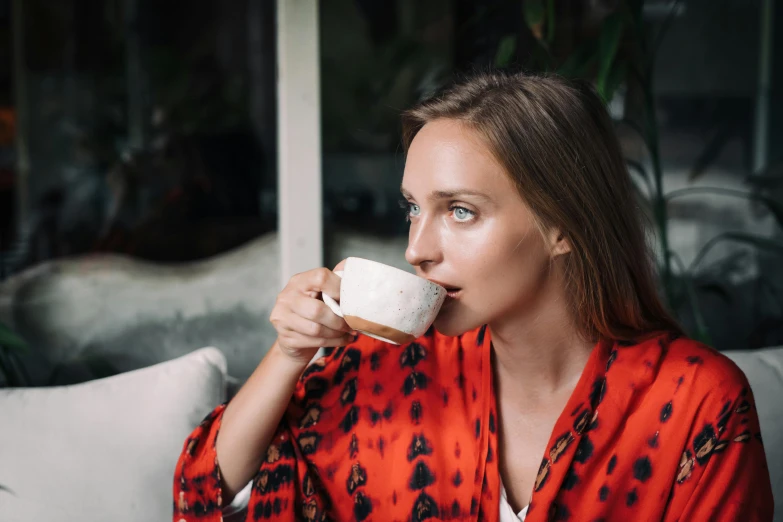 a woman sitting on a couch drinking a cup of coffee, a portrait, by Julia Pishtar, pexels contest winner, happening, orange robe, aussie baristas, portrait sophie mudd, al fresco