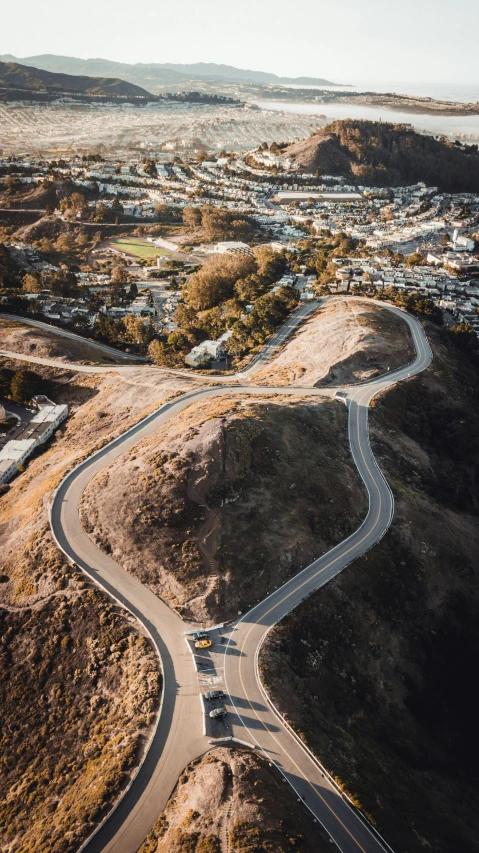 an aerial view of a winding road in the desert, by Josh Bayer, unsplash contest winner, overlooking sf from twin peaks, built on a steep hill, suburbs, postproduction