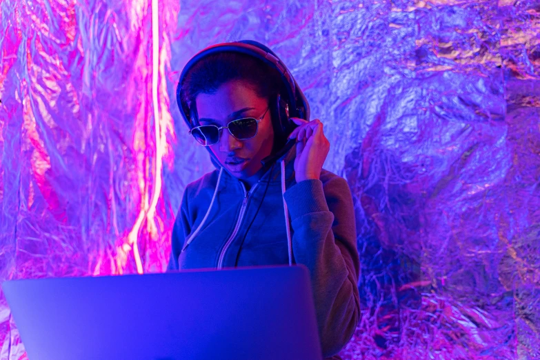 a woman sitting in front of a laptop wearing headphones, pexels, computer art, purple laser lighting, ashteroth, dj at a party, ambient cave lighting