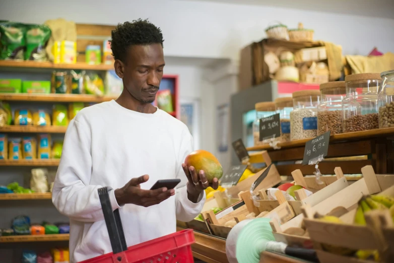 a man standing in a store looking at his cell phone, a photo, getting groceries, sustainability, dark-skinned, a brightly coloured