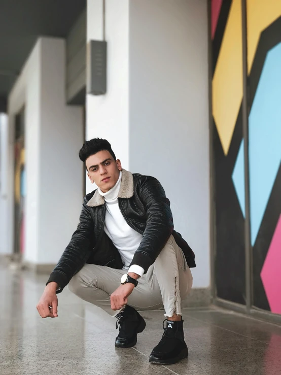 a man sitting on the ground in front of a colorful wall, trending on pexels, wearing a black leather jacket, shabab alizadeh, at college, profile image