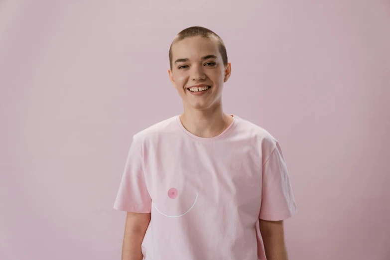 a young man standing in front of a pink wall, a character portrait, pexels contest winner, happening, genderless, wearing a t-shirt, she is smiling, shaved