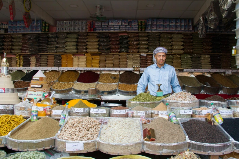 a man standing in front of a store filled with lots of food, spices, hicham habchi, grey, thumbnail