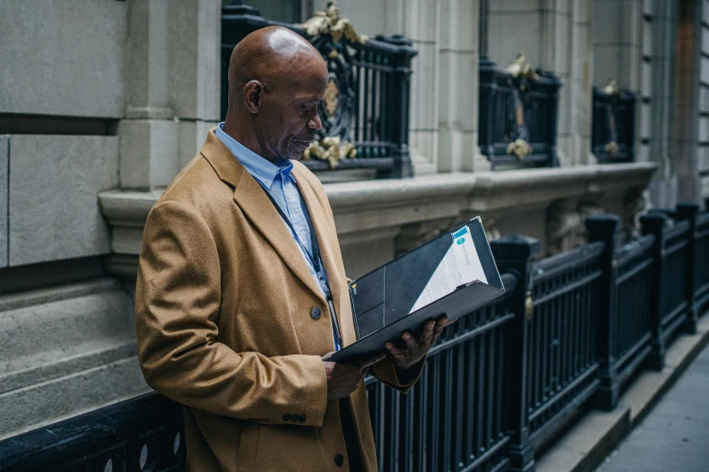 a man standing on a sidewalk reading a book, by Joseph Severn, pexels contest winner, black man, humans of new york style, holding grimoire, family photo