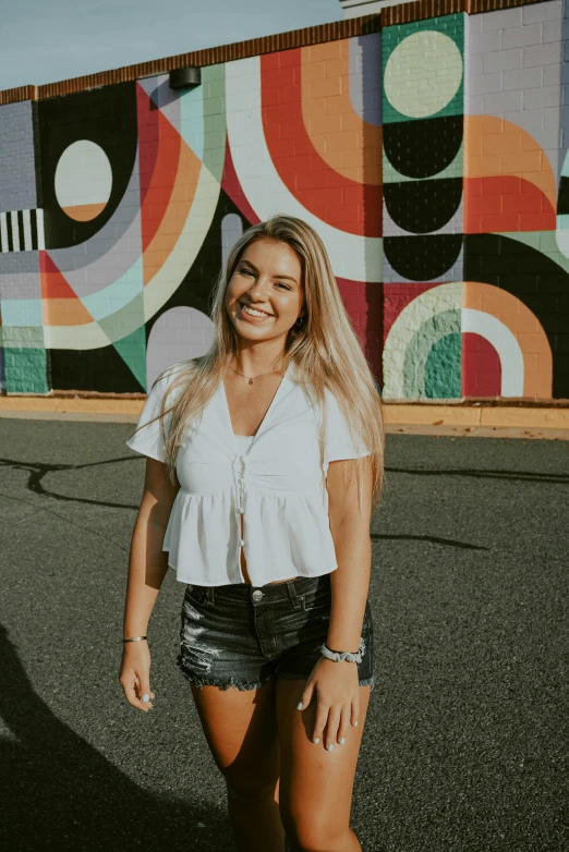 a woman standing in front of a colorful wall, a black and white photo, inspired by Sydney Carline, wearing a cropped tops, smiling young woman, trending photo, slightly tanned