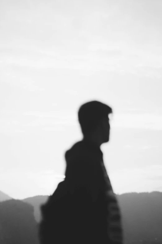 a black and white photo of a man with a backpack, a black and white photo, by Alexis Grimou, unsplash, silhouette :7, blurred photo, hills in the background, teenage boy