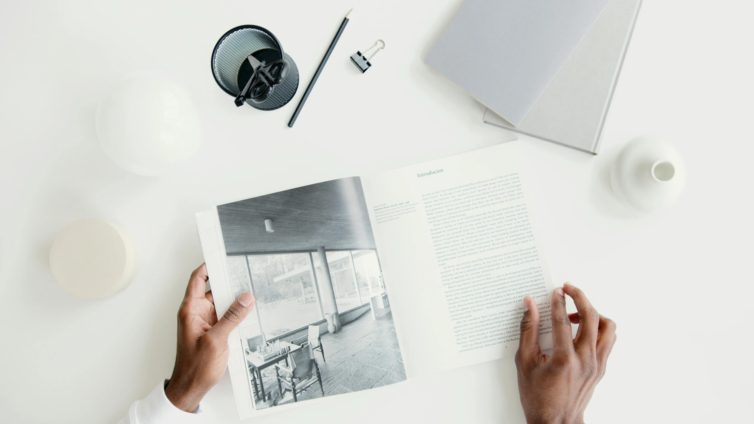 a person reading a book on a table, by Harvey Quaytman, unsplash contest winner, on white paper, architect, holding it out to the camera, scandinavian design