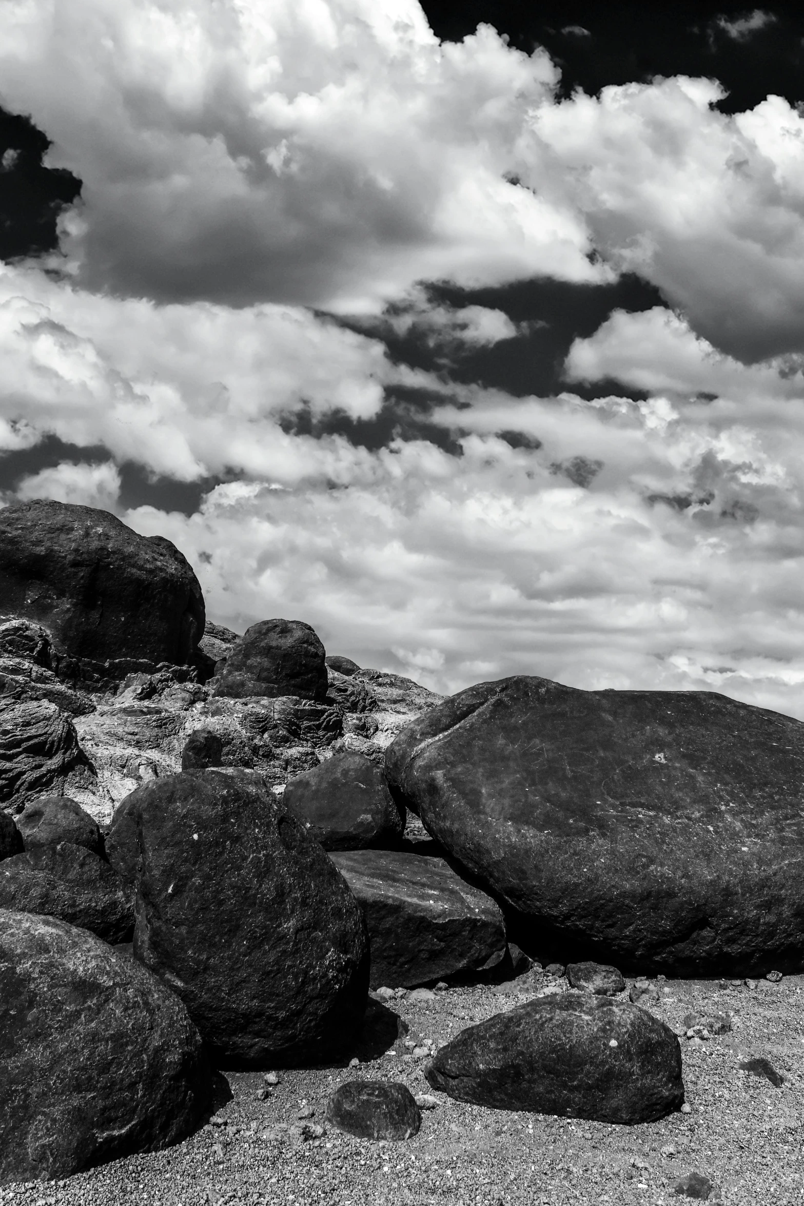 a black and white photo of rocks on a beach, inspired by Ansel Adams, visual art, puffy clouds, orange rocks, street photo, new mexico