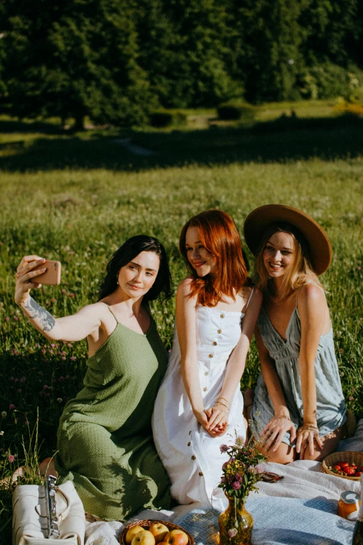 a group of women sitting on top of a grass covered field, taking a selfie, redhead woman, ready to model, three women