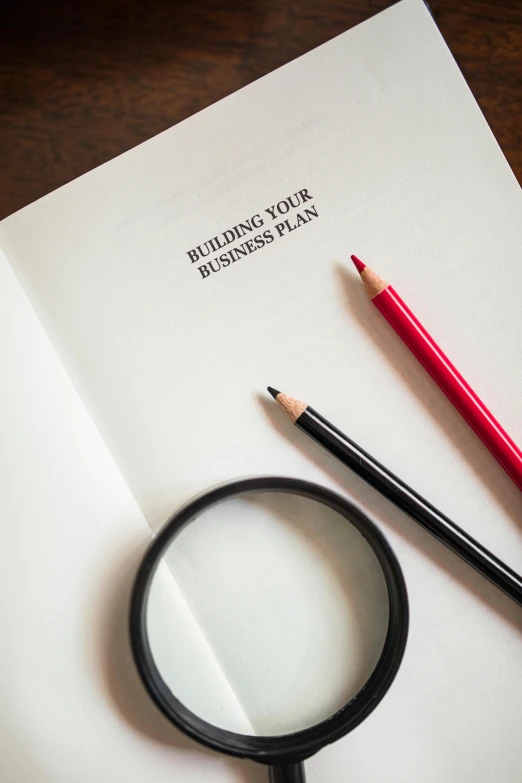 a magnifying glass sitting on top of a piece of paper, pencils, thumbnail, business, digital image