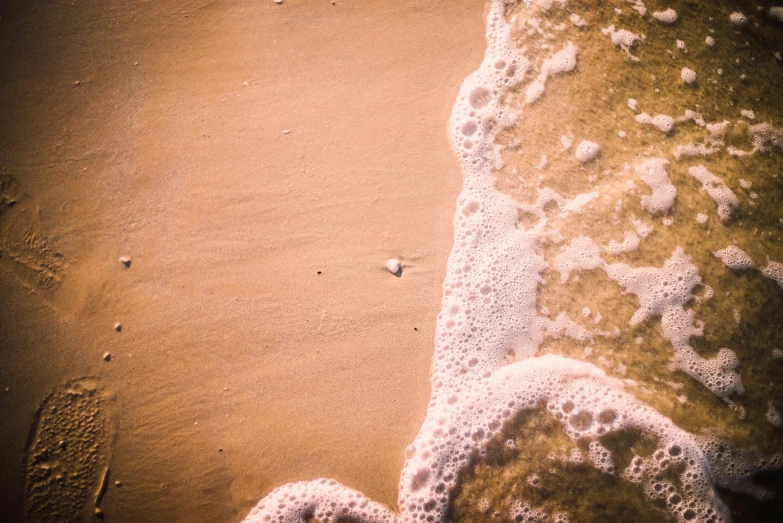 a person standing on top of a beach next to the ocean, inspired by Elsa Bleda, pexels contest winner, figuration libre, sea foam, birdseye view, sandy colours, floating alone