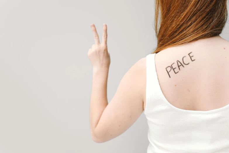 a woman with a peace sign tattooed on her back, trending on pexels, on a pale background, photographed for reuters, pale - skinned, celebrating