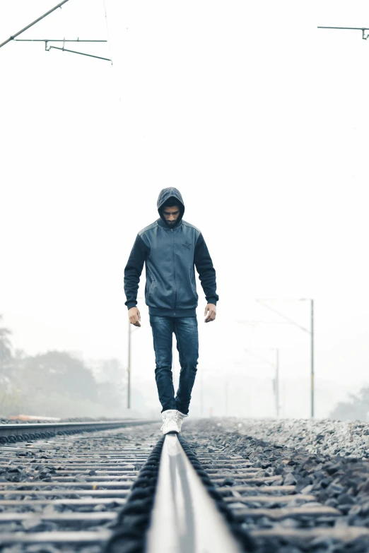 a man walking down a train track on a foggy day, wearing jeans and a black hoodie, upset, wearing a grey hooded sweatshirt, blue hoodie