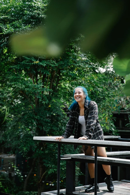 a woman with blue hair sitting on a bench, sumatraism, vibrant greenery, flannel, sitting on top a table, looking happy